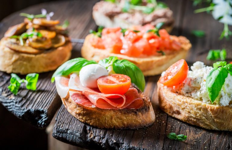 Bunte Bruschetta mit Tomaten, Schinken und frischem Basilikum auf Holzbrett.