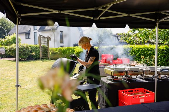 Frau grillt auf einer Außenveranstaltung mit Rauch im Hintergrund.