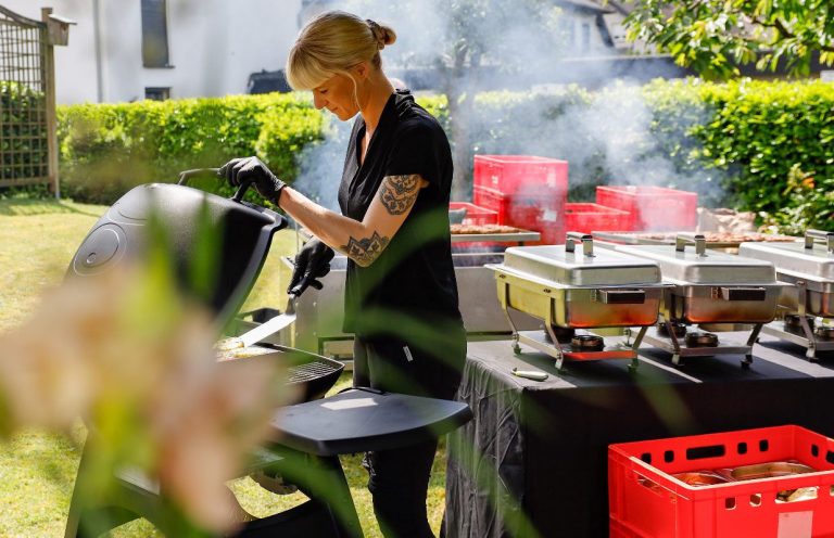 Frau grillt im Garten, umgeben von Rauch und Catering-Equipment.