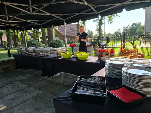 Buffet mit Speisen, Getränken und Besteck unter einem Zelt im Freien.