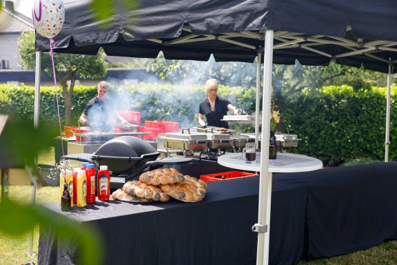 Grillstation im Freien mit Rauch, Tischen und vorbereiteten Speisen.
