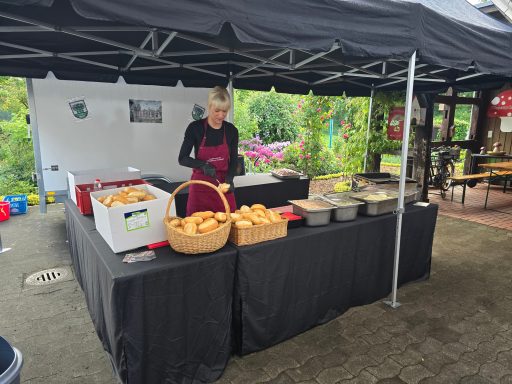 Marktstand mit Frau, die frisches Brot und Snacks verkauft, umgeben von Blumen.