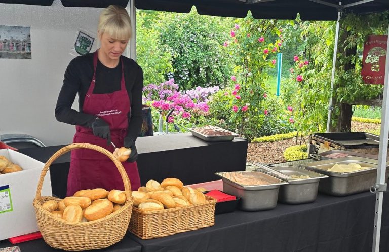 Verkäuferin in einem Stand, die Brötchen in einen Korb legt, umgeben von Speisen.
