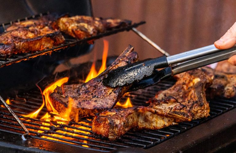 Gegrilltes Fleisch mit Flammen und einer Zange auf dem Grill.