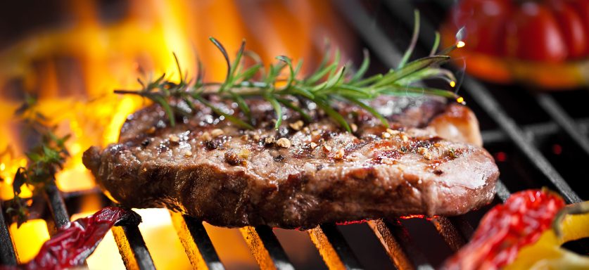 Saftiges Steak mit Gewürzen und frischem Rosmarin auf einem Grill.