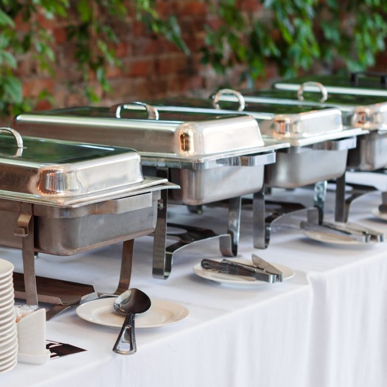 Buffet mit mehreren Warmhaltegefäßen auf einem gedeckten Tisch.