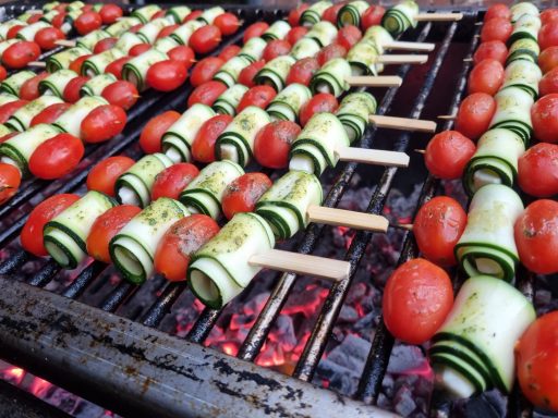 Gemüsespieße aus Zucchini und Tomaten, grillend über glühenden Kohlen.