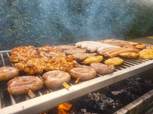 Gegrilltes Fleisch und Würstchen auf einem Grill, umgeben von Rauch.